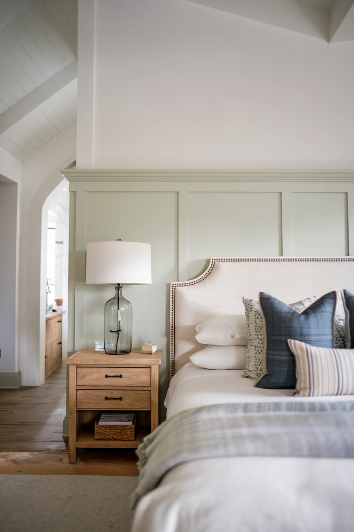 Modern farmhouse bedroom with white bedding and light green wainscoting, white walls