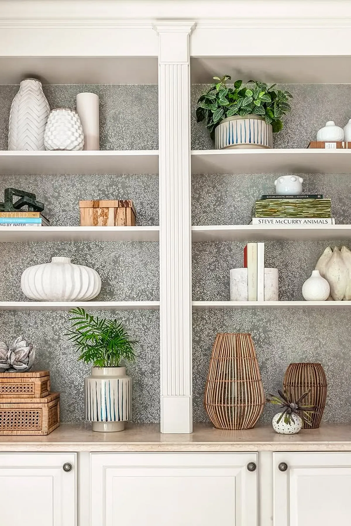Stylish shelves featuring white ceramics, green plants, wooden boxes, and a textured gray background.